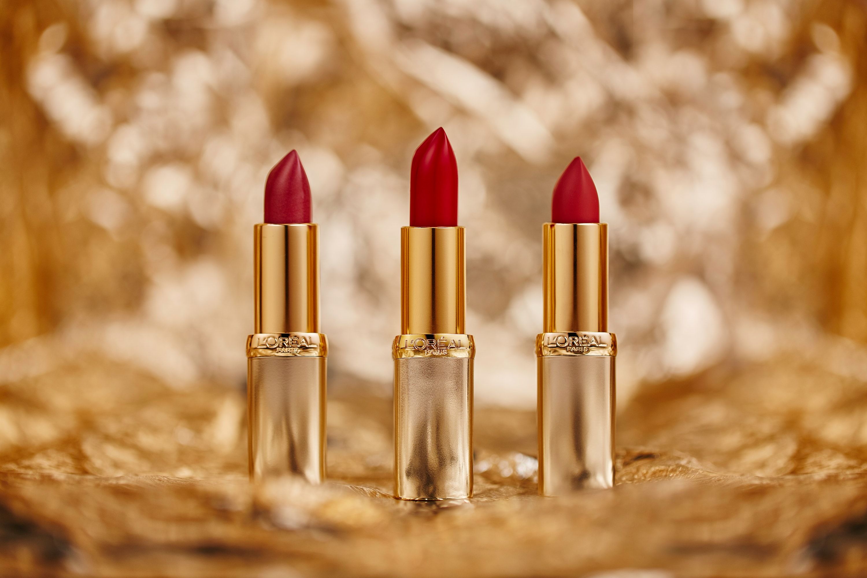 Trzy pomadki L'Oréal w złotych opakowaniach na złotym tle bokeh