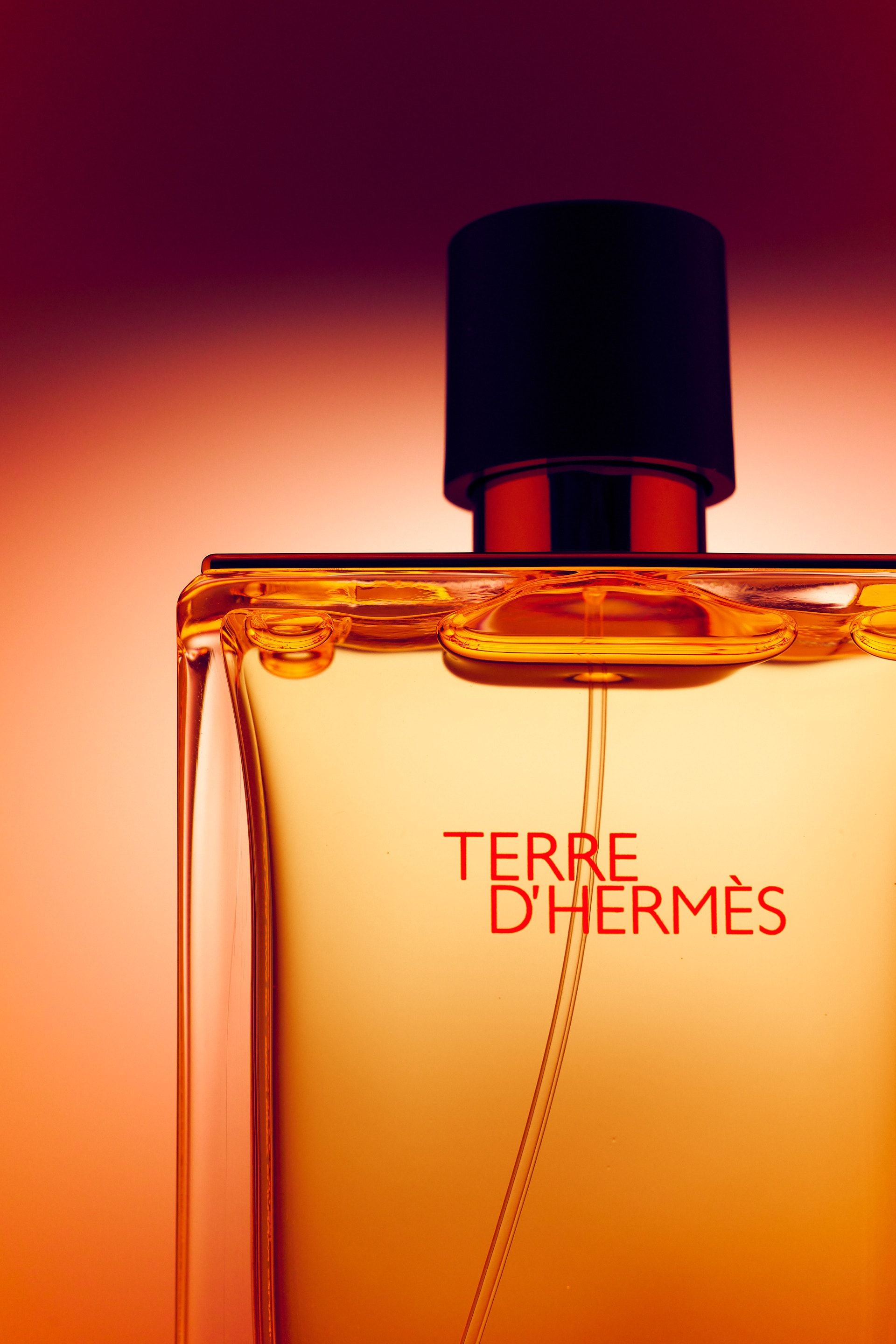 Flakon Terre d'Hermès na tle przechodzącym od bordo do pomarańczu