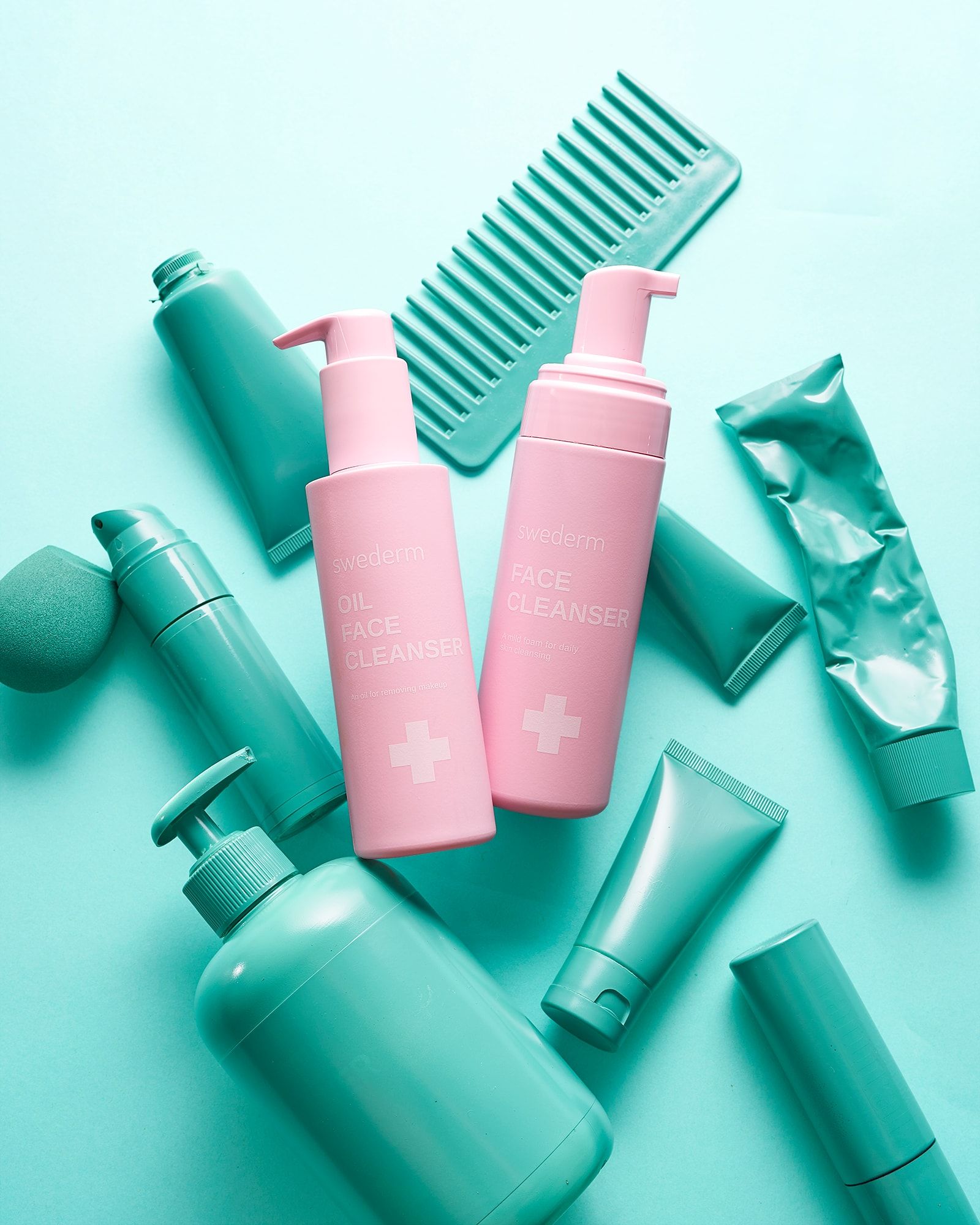 Różowe butelki Face Cleanser wśród miętowych kosmetyków i grzebienia na miętowym tle