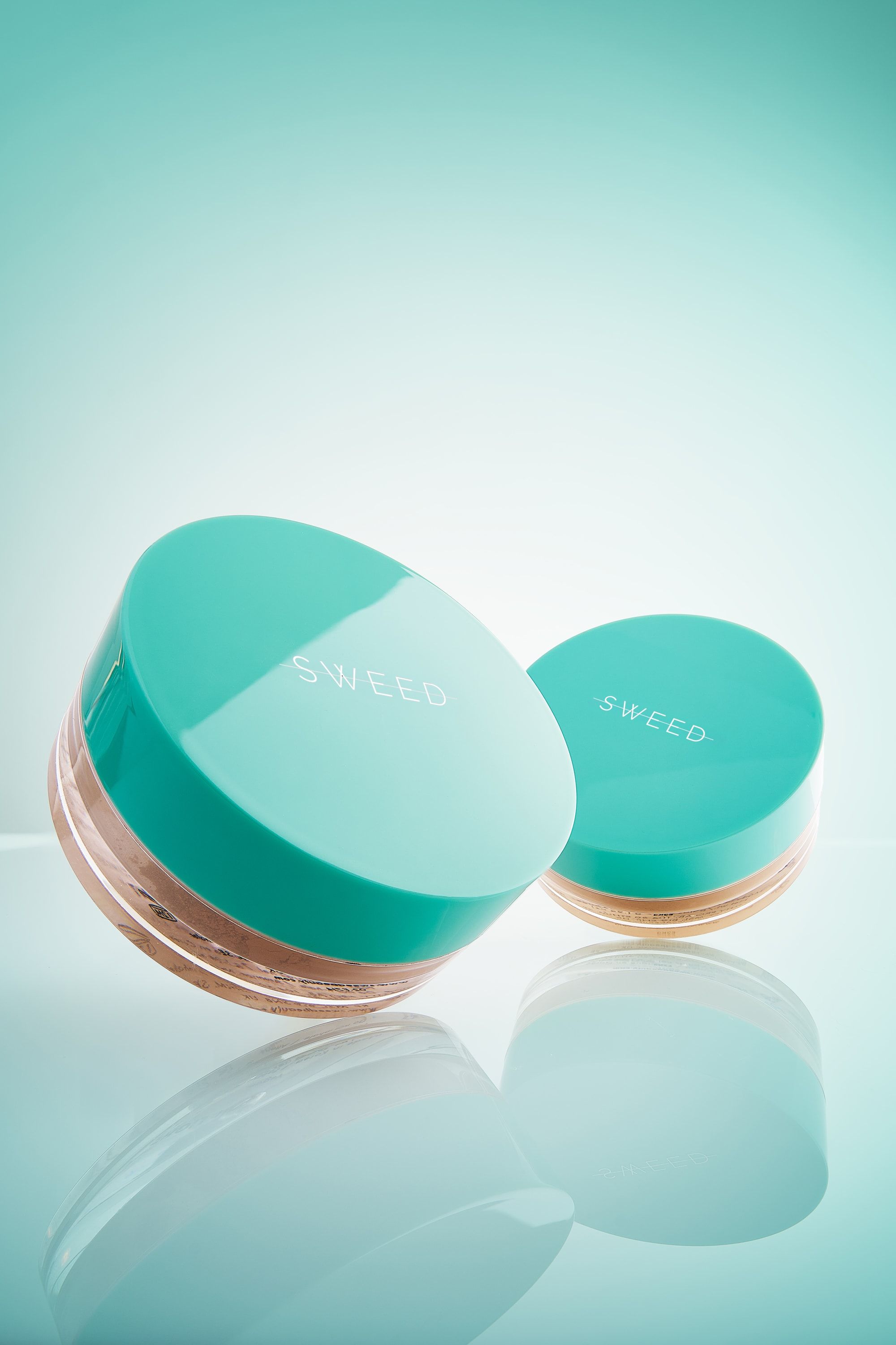 Dwa słoiczki pudru sypkiego Sweed z miętowymi wieczkami, przechylone, z odbiciem w szkle
