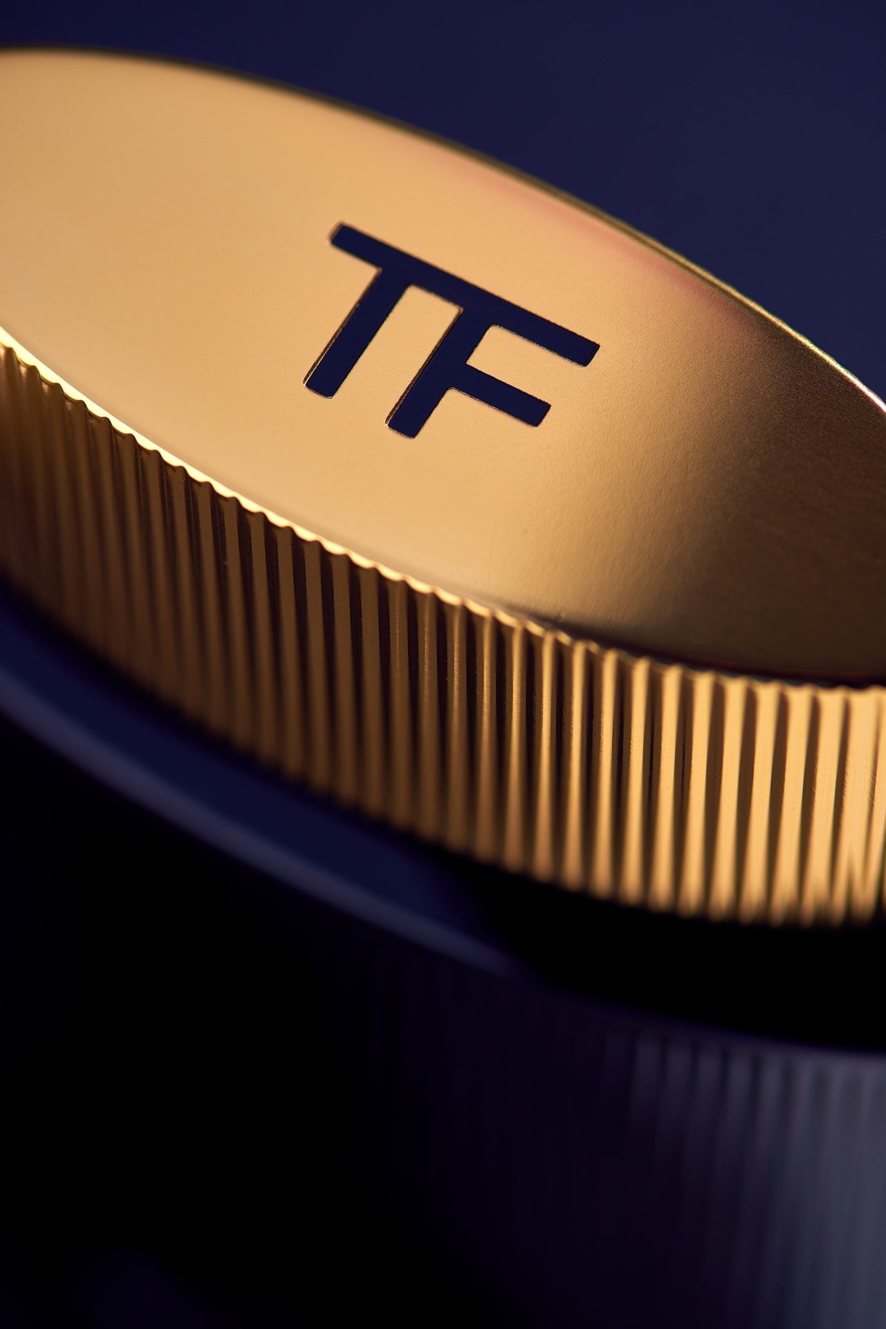 Złota nakrętka perfum Tom Ford z bliska na granatowym tle