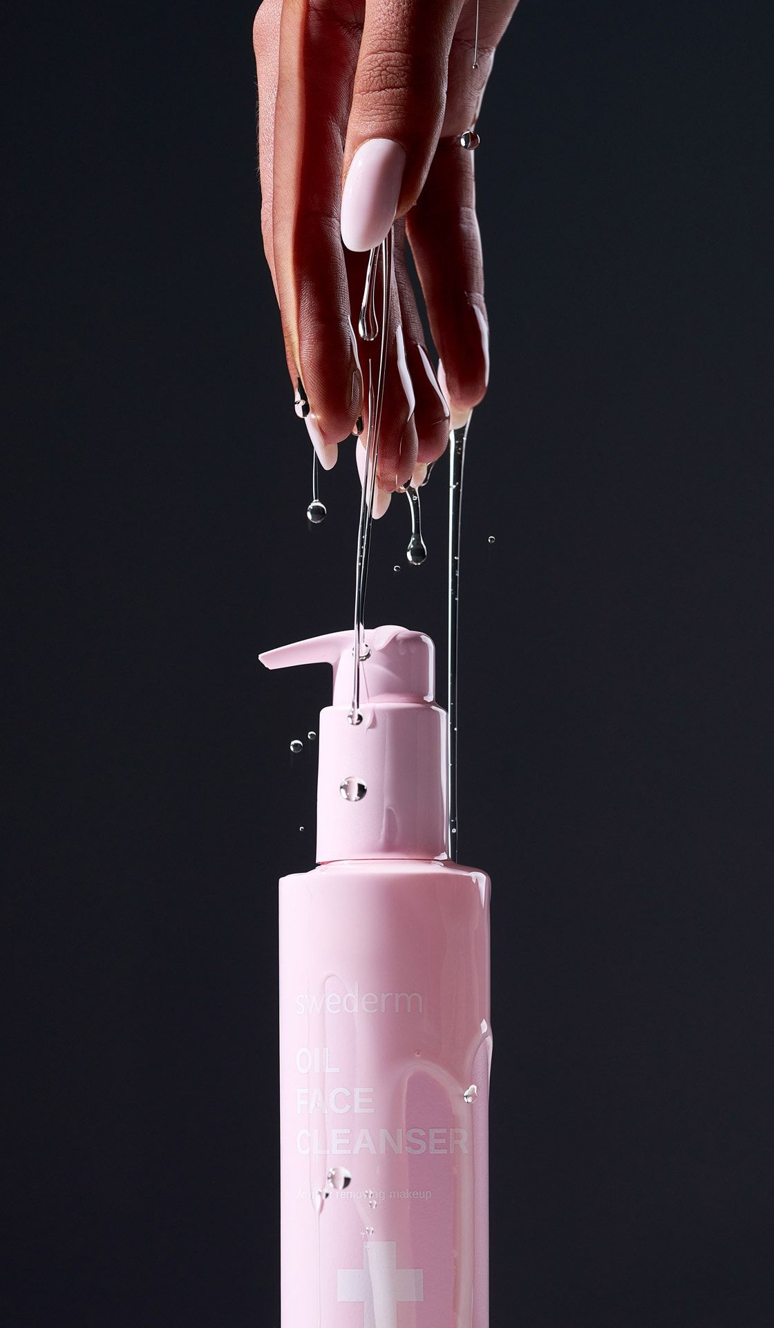 Dłoń ociekająca olejkiem nad różową butelką Oil Face Cleanser