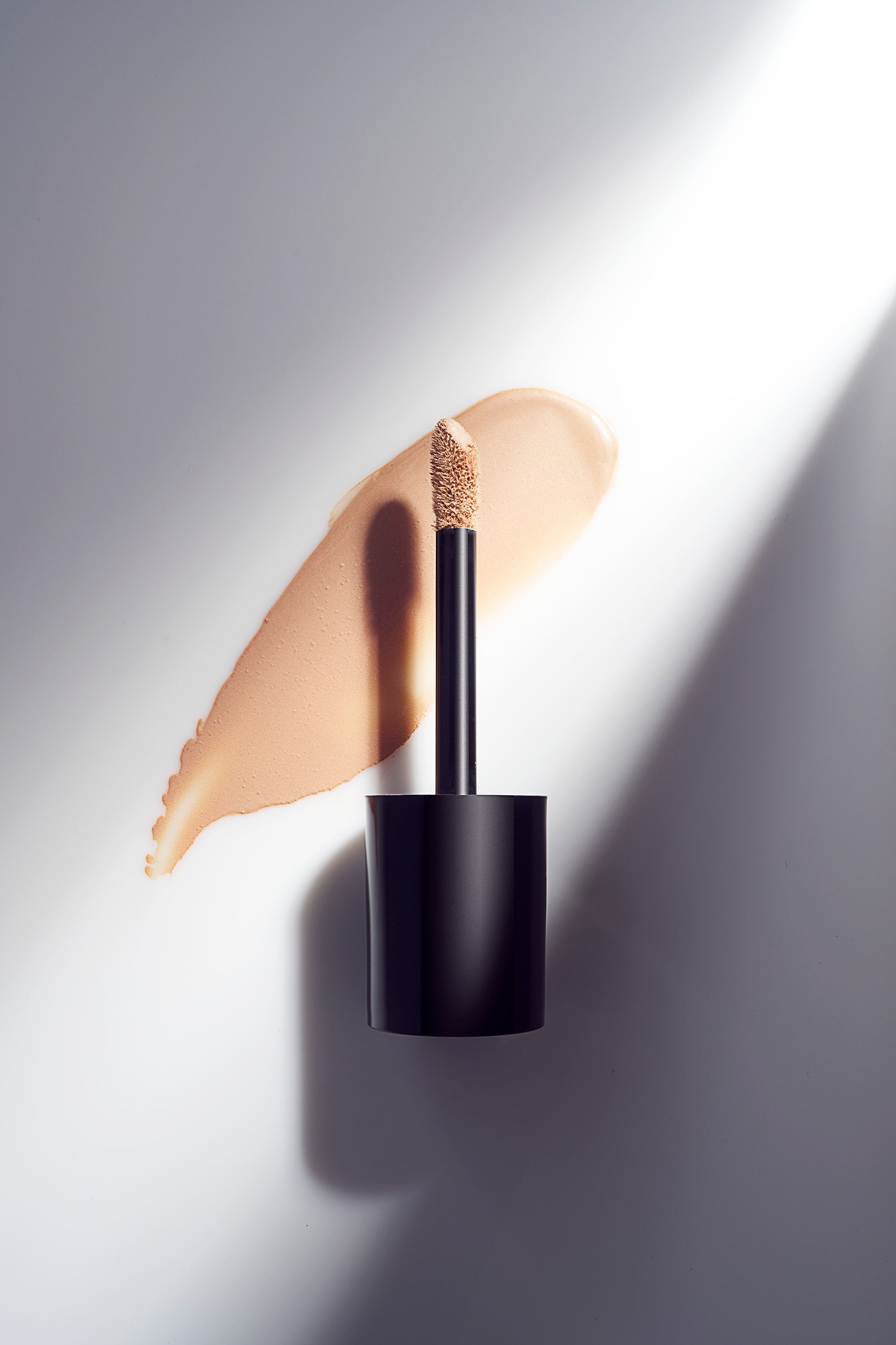 Aplikator z kroplą podkładu i swatch na jasnym tle w ostrym świetle