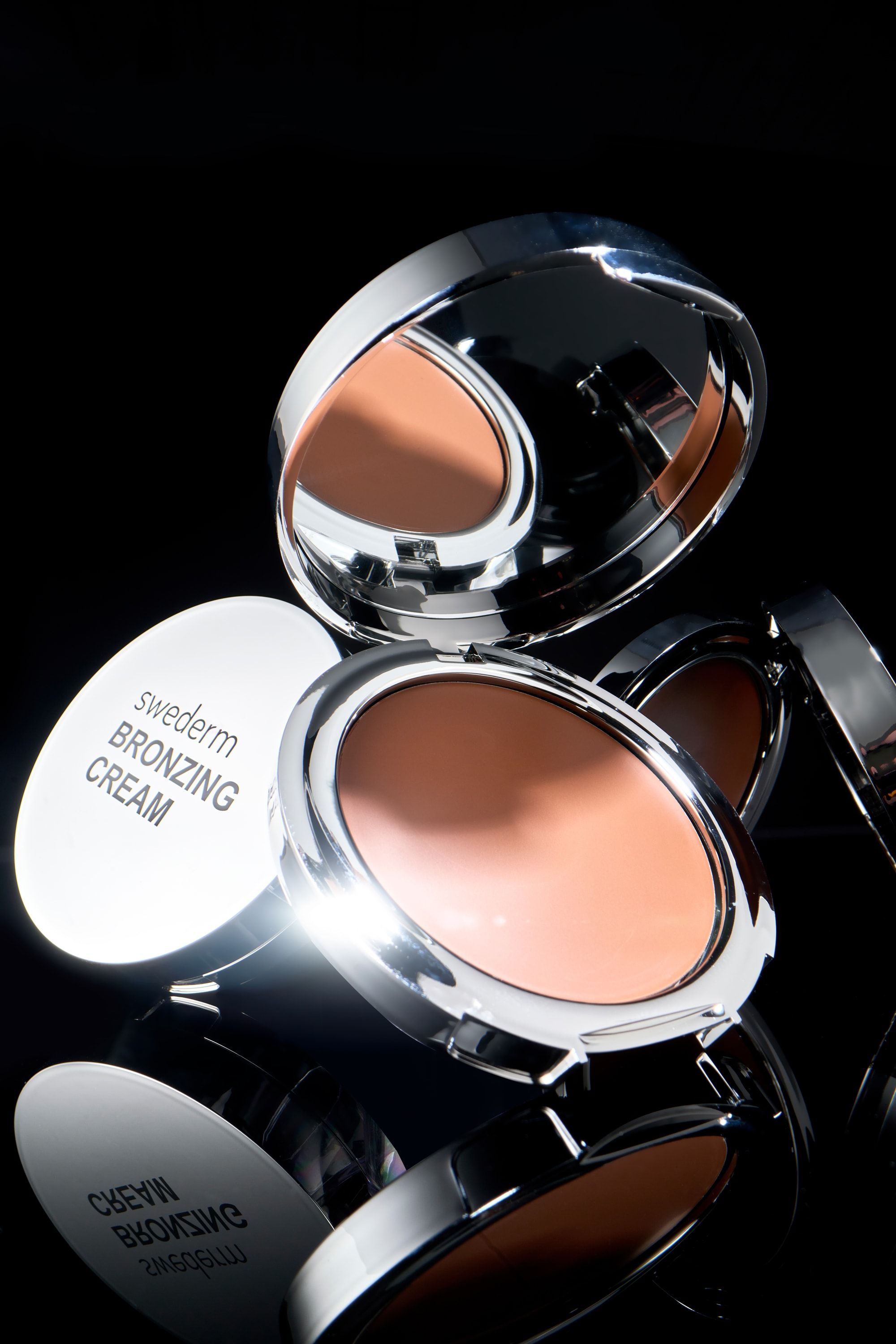 Otwarte puderniczki Swederm Bronzing Cream w ostrym świetle na czarnym tle