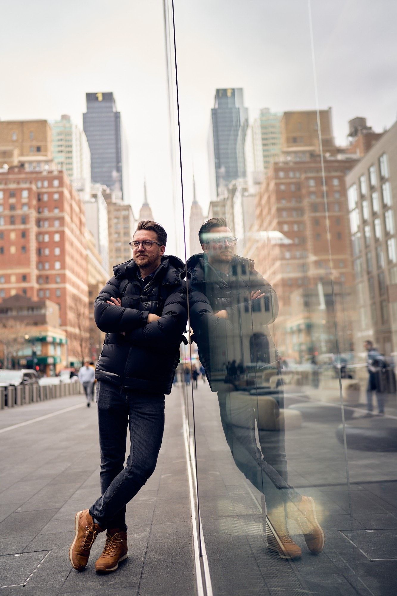 Marcin Sowa, fotograf i dyrektor kreatywny, opiera się o szklaną ścianę na Manhattanie, w tle Empire State Building